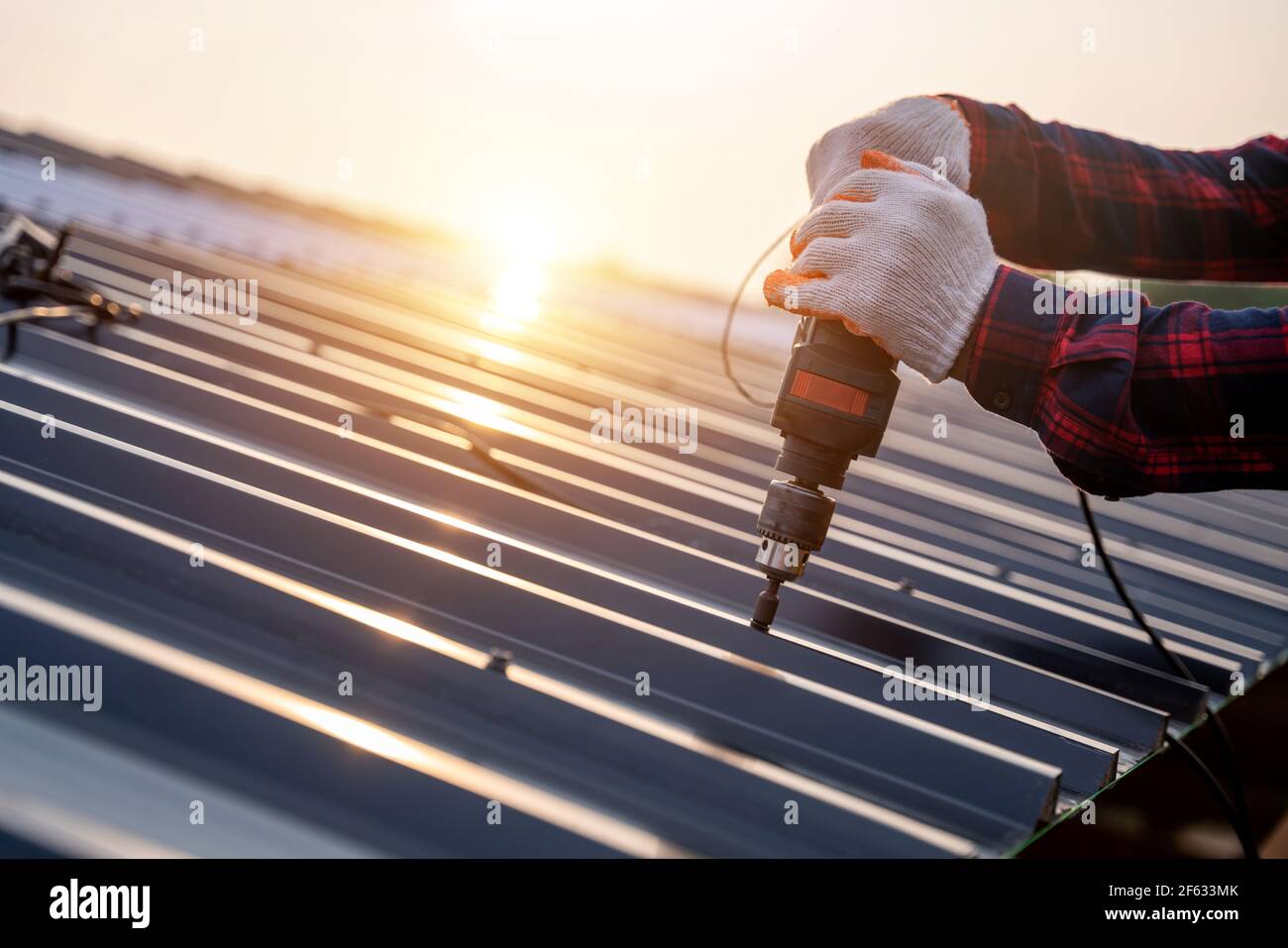 Nahaufnahme Hand der Bauarbeiter Sicherheitsverschleiß mit elektrischen Bohrwerkzeugen auf dem neuen Dach Metallblech installieren, Dachkonstruktion Konzept. Stockfoto