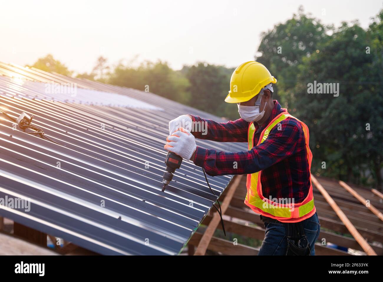 Asiatische Bauarbeiter Sicherheitsverschleiß mit elektrischen Bohrwerkzeugen installieren auf dem neuen Dach Metallblech, Dachkonstruktion Konzept. Stockfoto