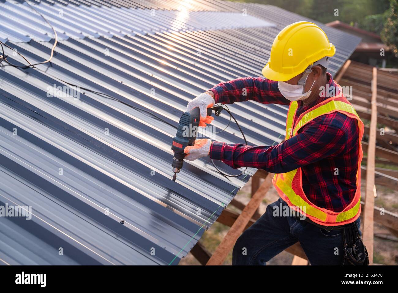 Draufsicht Bauarbeiter Sicherheitsverschleiß mit elektrischen Bohrwerkzeugen auf neuem Dach Metallblech installieren, Dachkonstruktion Konzept. Stockfoto