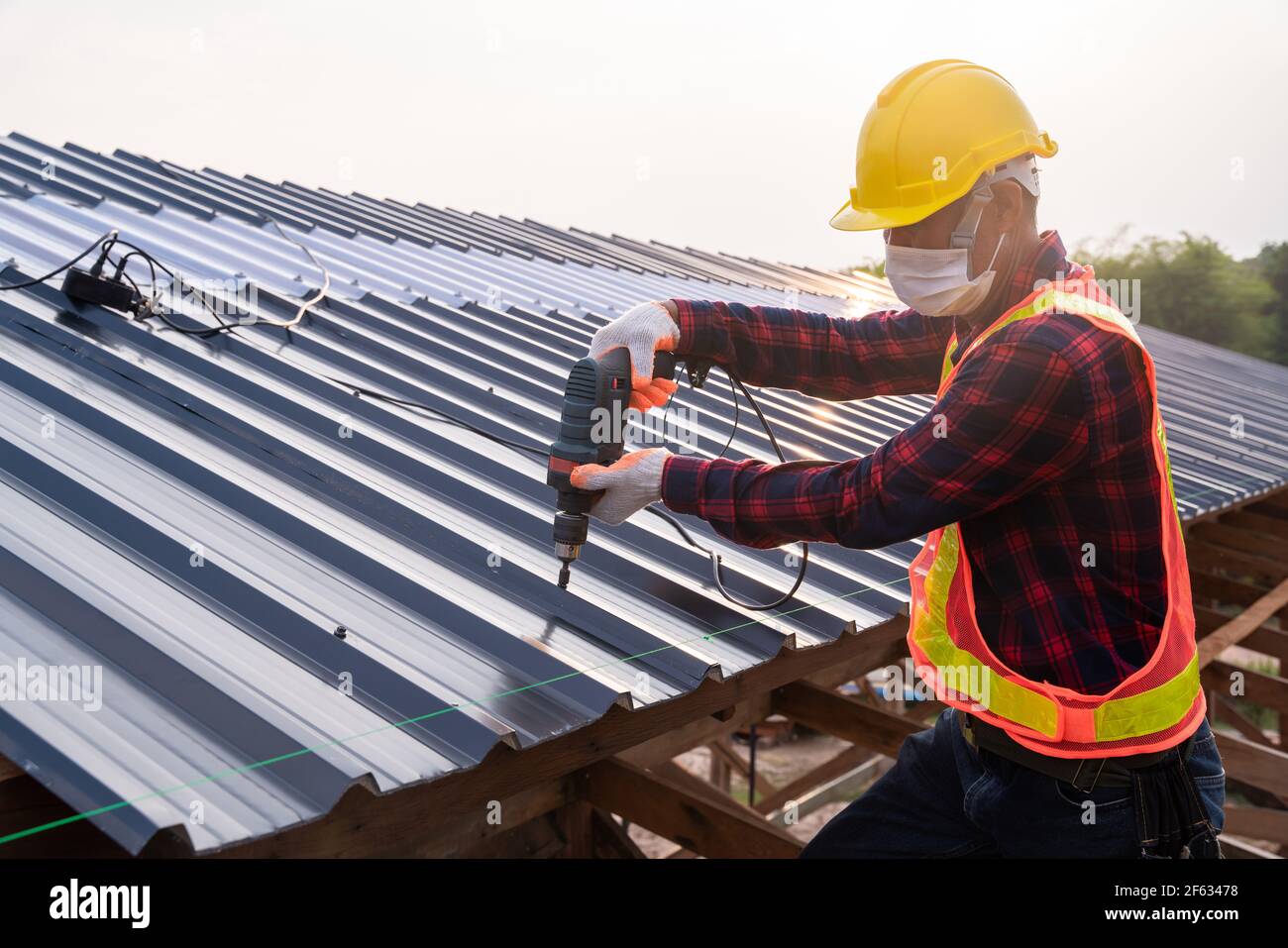 Sicherheitsverschleiß der Bauarbeiter mit elektrischen Bohrwerkzeugen installieren auf neuem Dachblech, Dachkonstruktion Konzept. Stockfoto