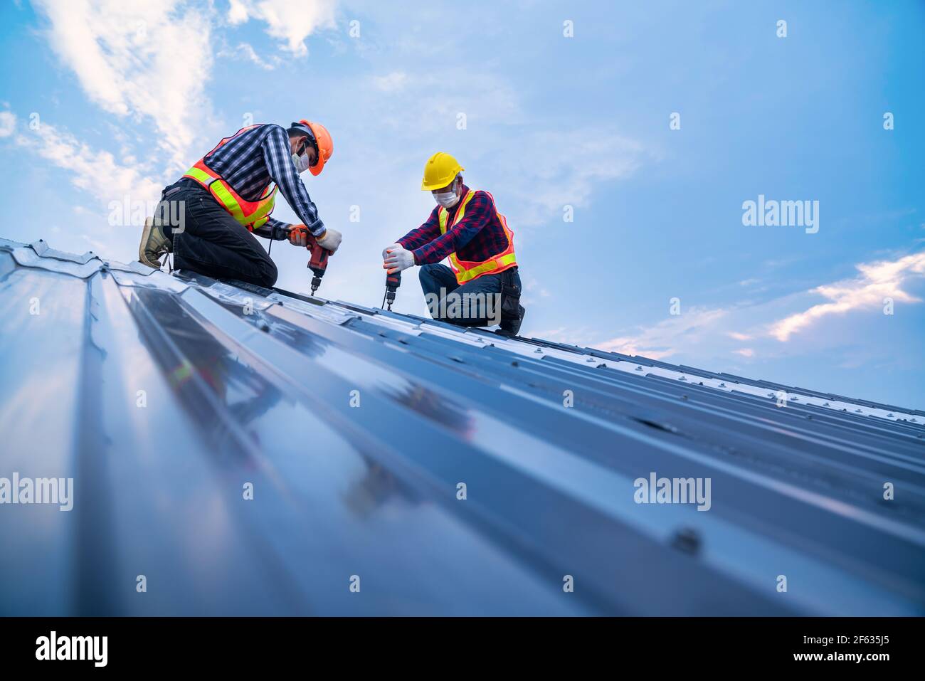Abschleppkonstruktion Sicherheitsverschleiß mit elektrischen Bohrwerkzeugen installieren auf dem neuen Dach Metallblech, Dachkonstruktion Konzept. Stockfoto