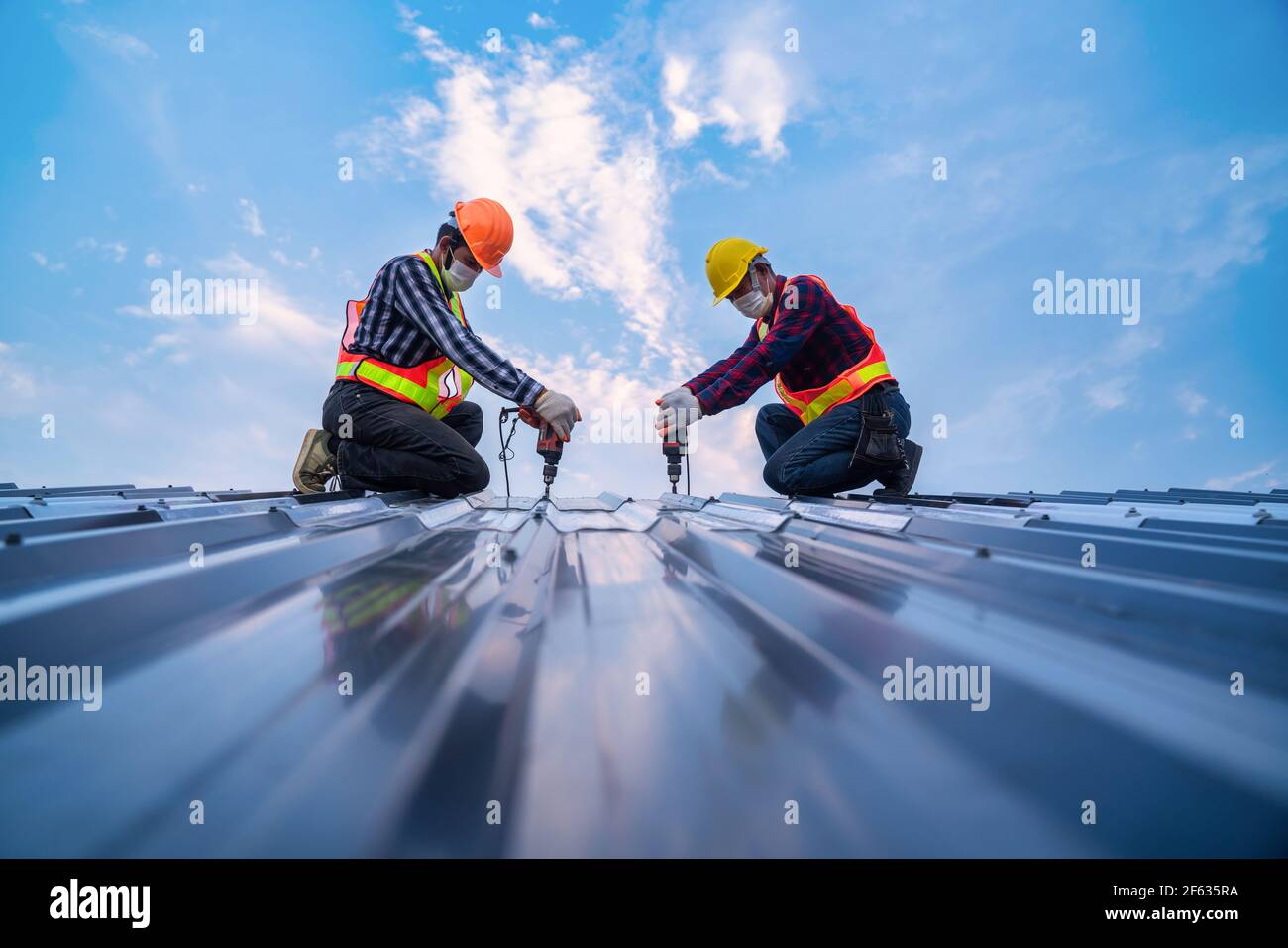 Teamarbeit Bauarbeiter Sicherheitsverschleiß mit elektrischen Bohrwerkzeugen auf dem neuen Dach Metallblech installieren, Dachkonstruktion Konzept. Stockfoto