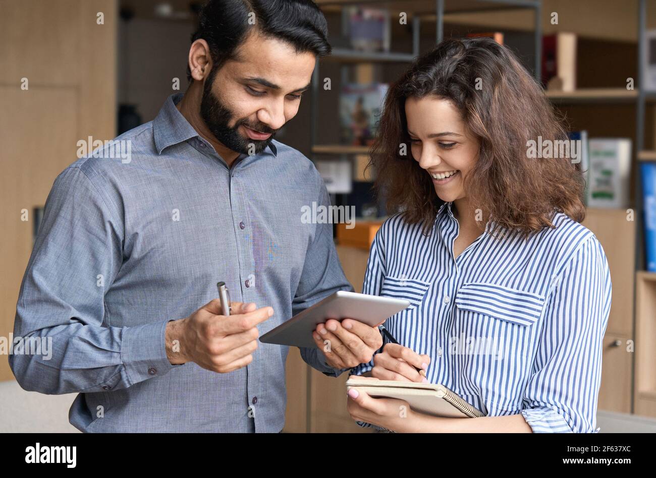 Indische und hispanische glückliche Kollegen sprechen mit digitalen Tablet im Büro. Stockfoto