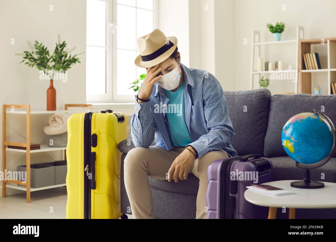 Mann sitzt auf dem Sofa zu Hause mit Koffer deprimiert über Seine abgesagten Reisepläne Stockfoto
