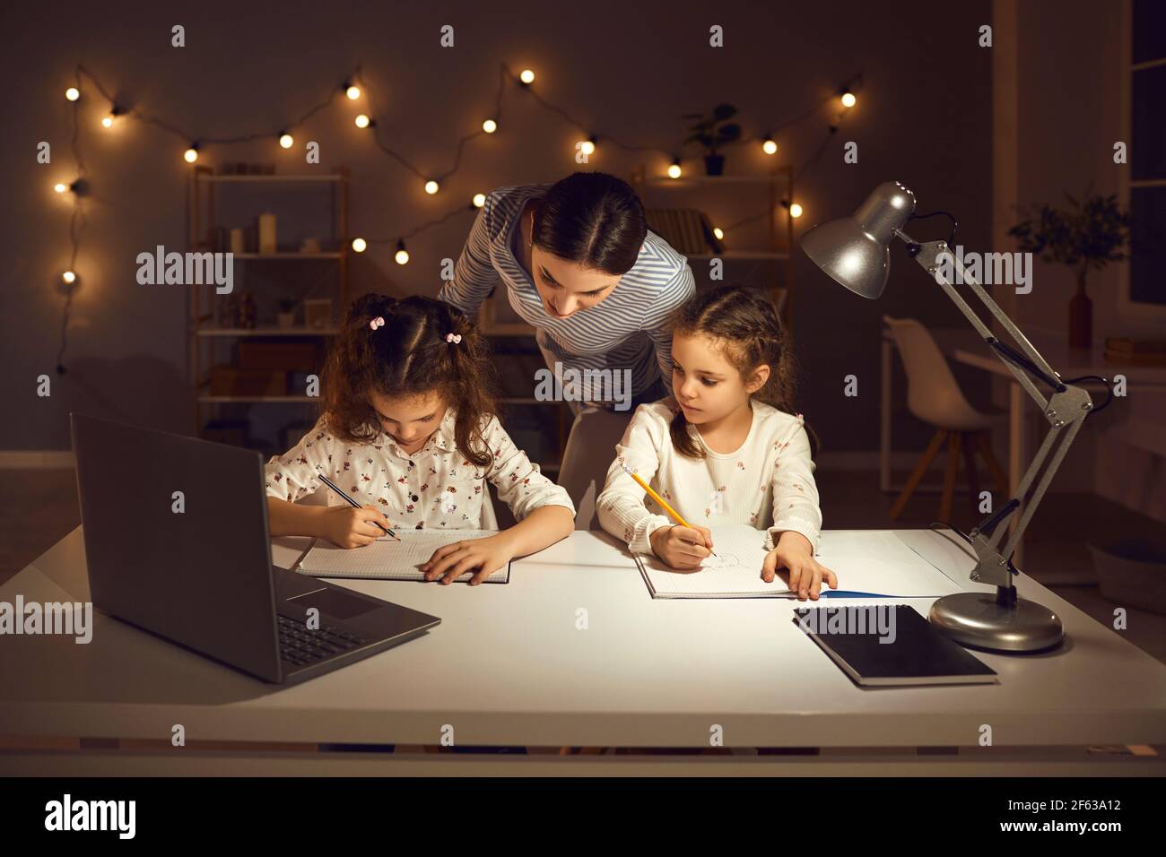 Junge Mutter hilft ihren kleinen Kindern mit Schulaufgaben spät Am Abend Stockfoto