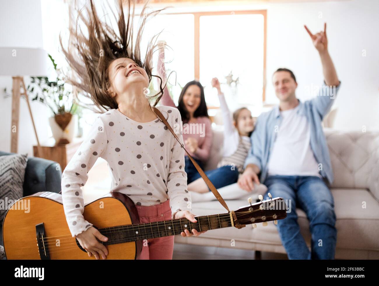 Kleines Mädchen mit Familie drinnen zu Hause, Spaß mit Gitarre. Stockfoto