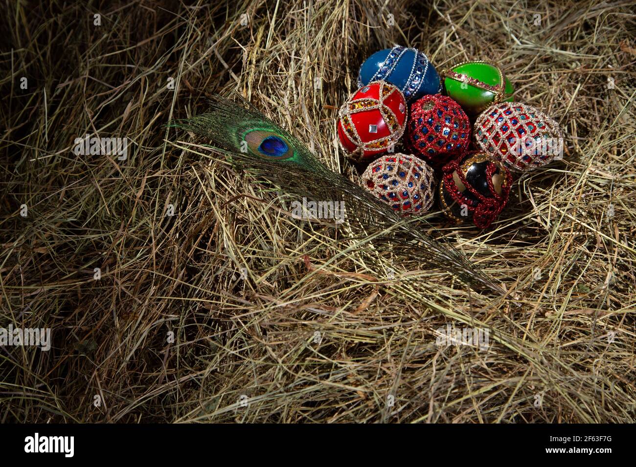 OSTEREIER ALS FABERGE-EIER IN EINEM STROHNEST DEKORIERT MIT PFAUENFEDER Stockfoto