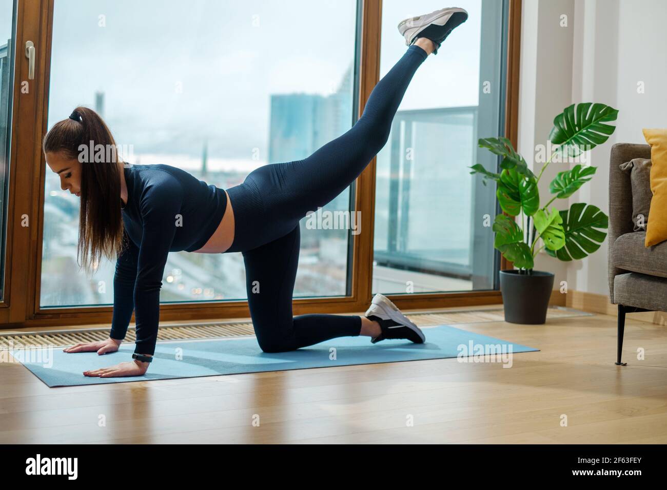 Frau praktiziert Körpergewichtsübungen in der Nähe des Panoramafensters Stockfoto