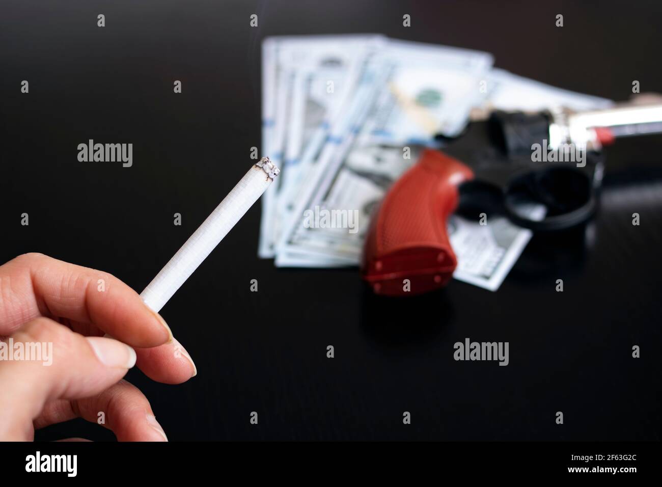 Pistole, Dollar und Hand mit einer Zigarette auf einem Holztisch Stockfoto