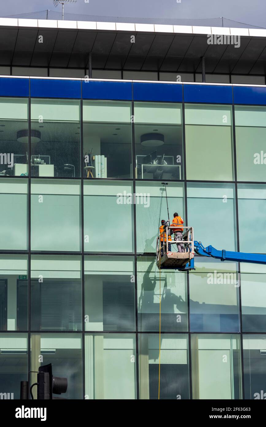 Fensterputzer, die hohe Bürofenster mit einer Kirschenpflücker-Plattform waschen. Arbeiter, die eine Luftarbeitsbühne benutzen, um auf hohe Gebäude zu gelangen. Wasserversorgte Stange Stockfoto