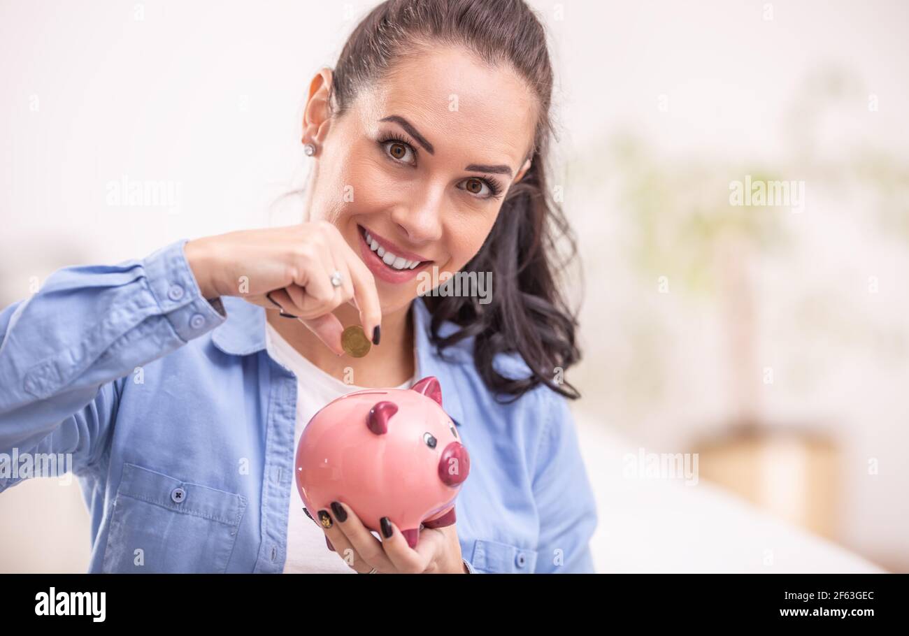 Geld sparen in ein rosa Sparschwein von einer Brünette Frau mit einer Kupfermünze. Stockfoto