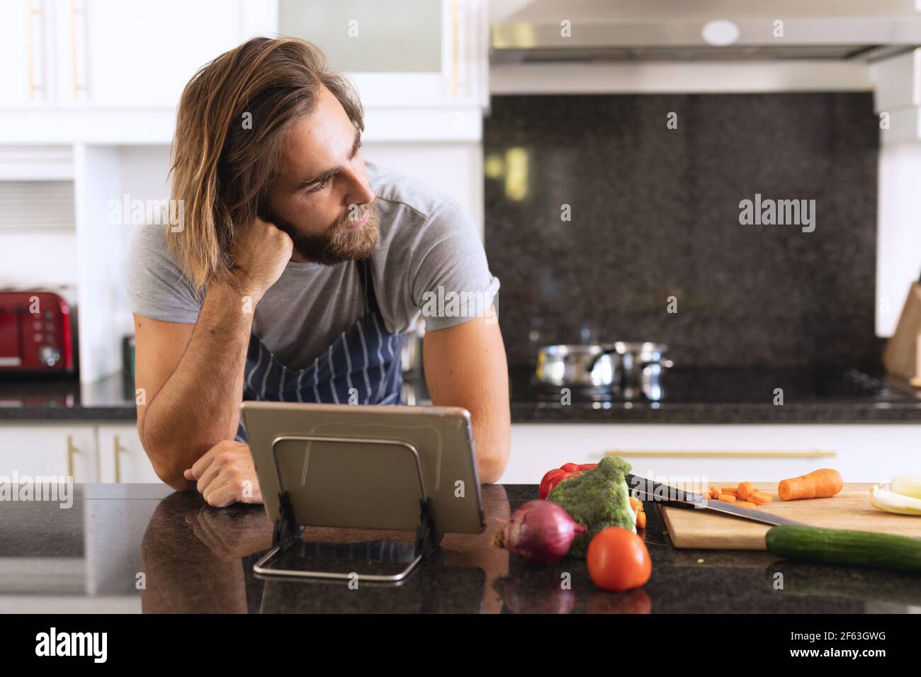 Kaukasischer Mann in der Küche trägt Schürze und Denken Stockfoto