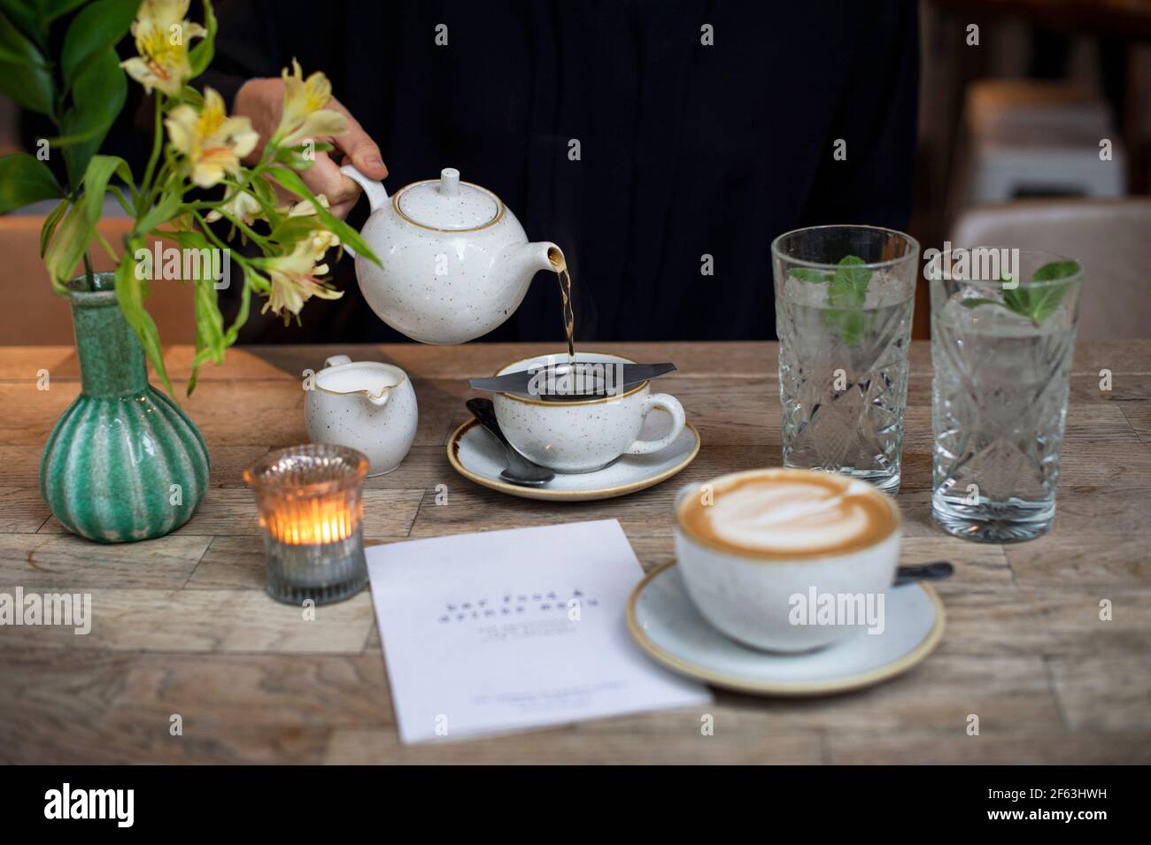 Weibliche Hand gießt Tee aus einer Teekannen im Restaurant. Lifestyle, Afternoon-Tea-Konzept. Leeres Papiermenü mit Kopierbereich. London, Großbritannien Stockfoto