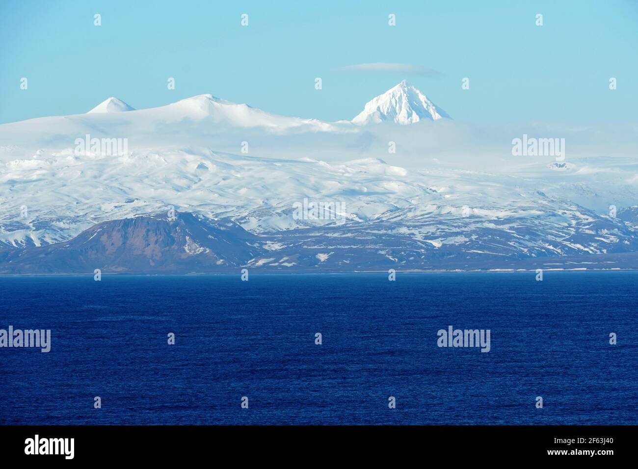 Schneebedeckte Berge auf den Aleutischen Inseln als Teil der Inselkette in Alaska, die von einem Containerschiff aus über den Pazifischen Ozean segelt. Stockfoto