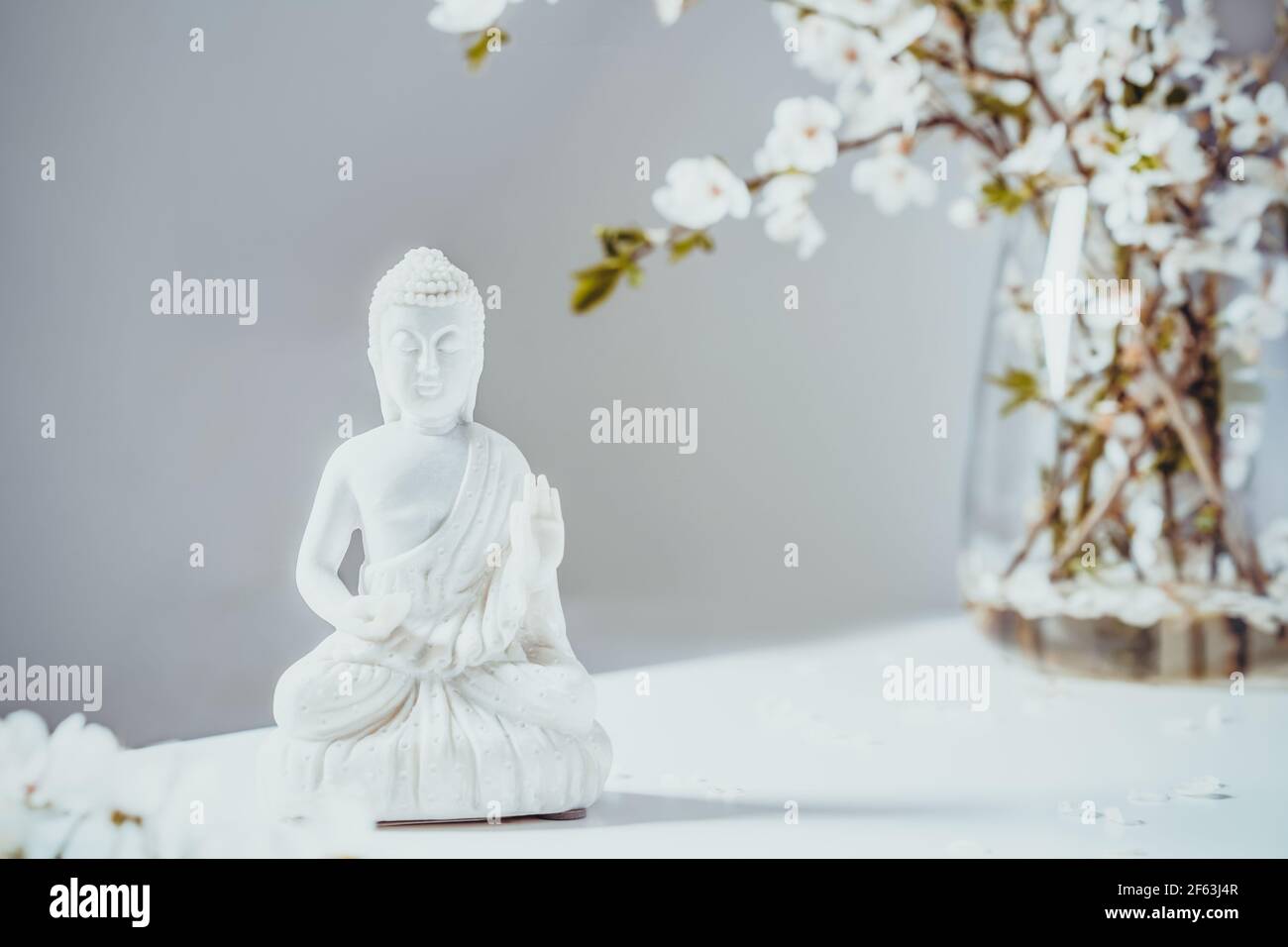 Dekorative weiße Buddha Statuette mit blutigen Ästen in der Vase auf weißem Hintergrund. Meditations- und Entspannungsritual. Buddha Geburtstag Stockfoto