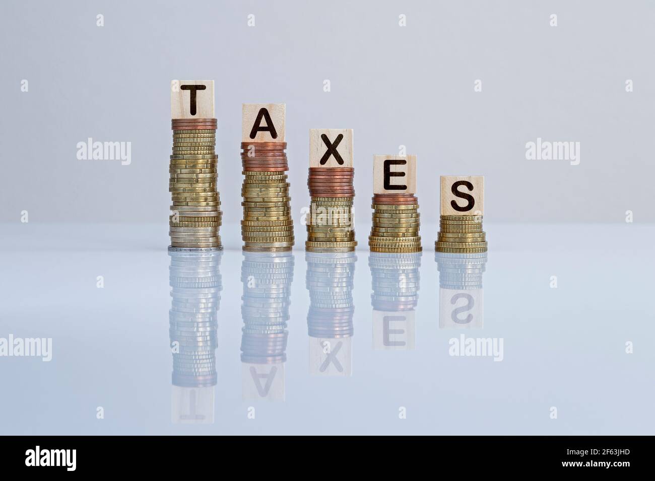 Wort „Steuern“ auf Holzblöcken auf absteigenden Münzstapeln vor grauem Hintergrund. Konzeptfoto von Steuersenkungen, Wirtschaft, Unternehmen und Finanzen. Stockfoto