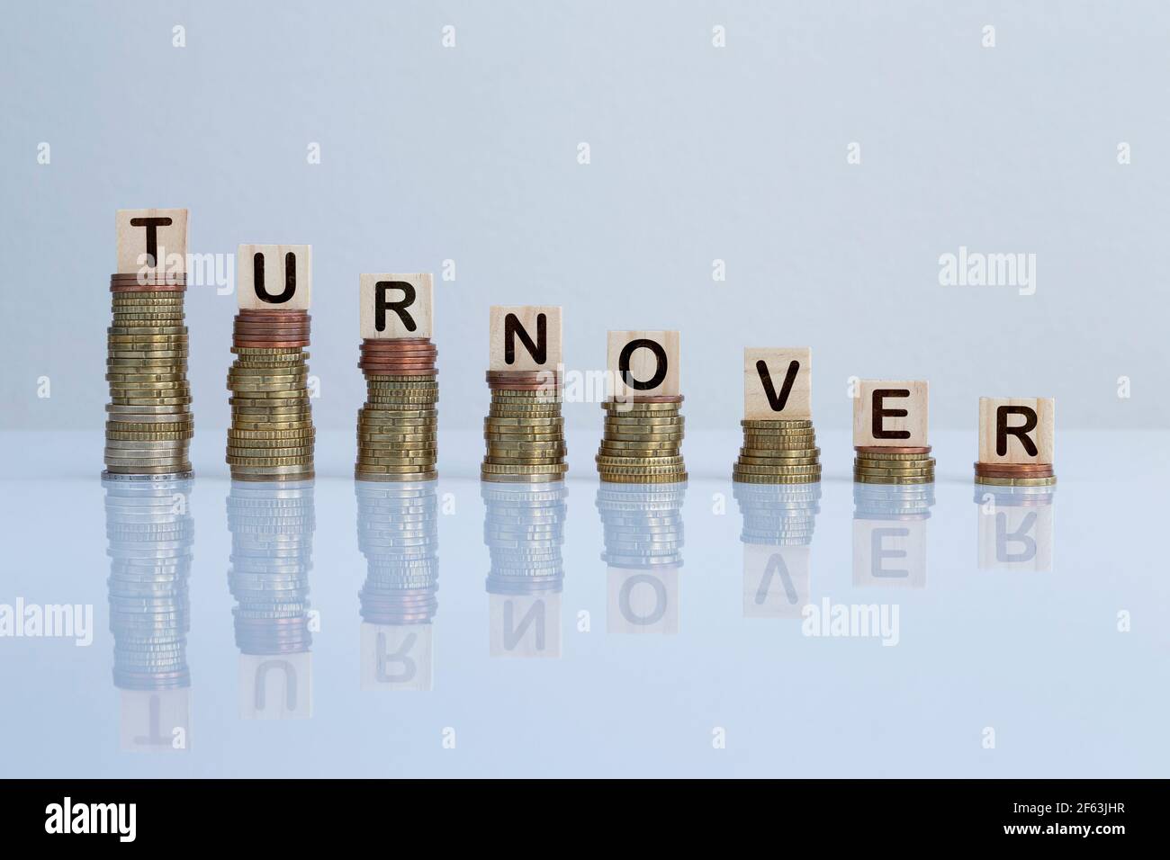Wort „UMSATZ“ auf Holzblöcken auf absteigenden Münzstapeln. Konzeptfoto von Geldverlust, Wirtschaftskrise, Rezession und finanzieller Reduktion. Stockfoto
