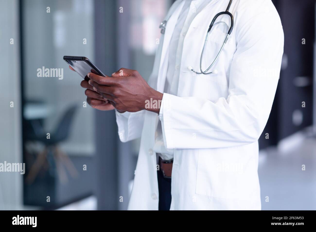 Mittelteil des afroamerikanischen männlichen Arztes mit weißem Mantel und Stethoskop mit digitalem Tablet Stockfoto