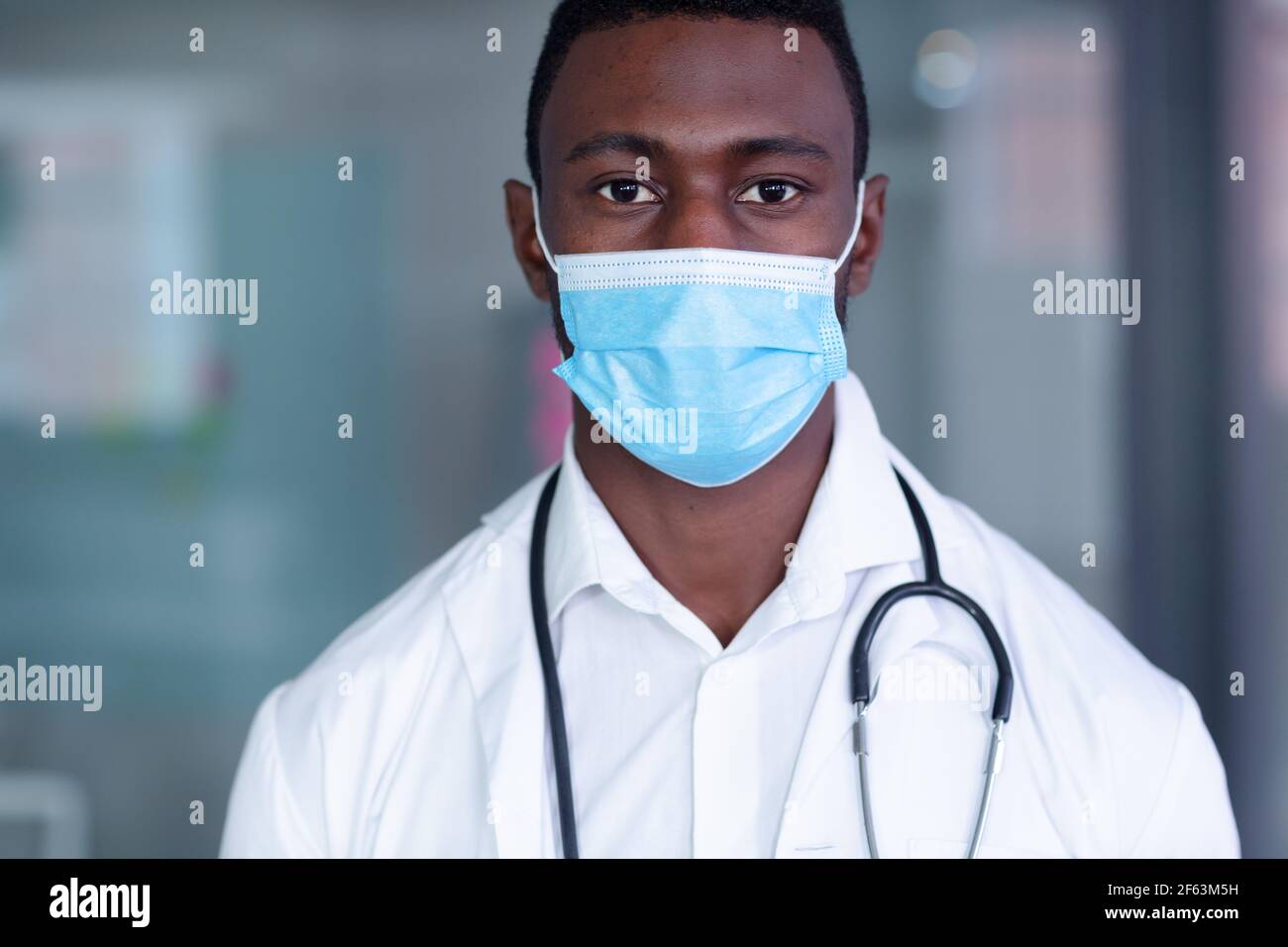 Porträt eines afroamerikanischen Arztes mit Gesichtsmaske, weißem Mantel und Stethoskop Stockfoto