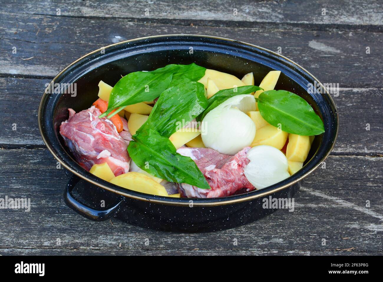 Rohe Lammsteaks in einem Topf, gewürzt und mit verschiedenen Sorten von kultiviertem und wildem Gemüse, Zwiebeln, Kartoffeln, Karotten und Ramson, bereit zu sein angeordnet Stockfoto