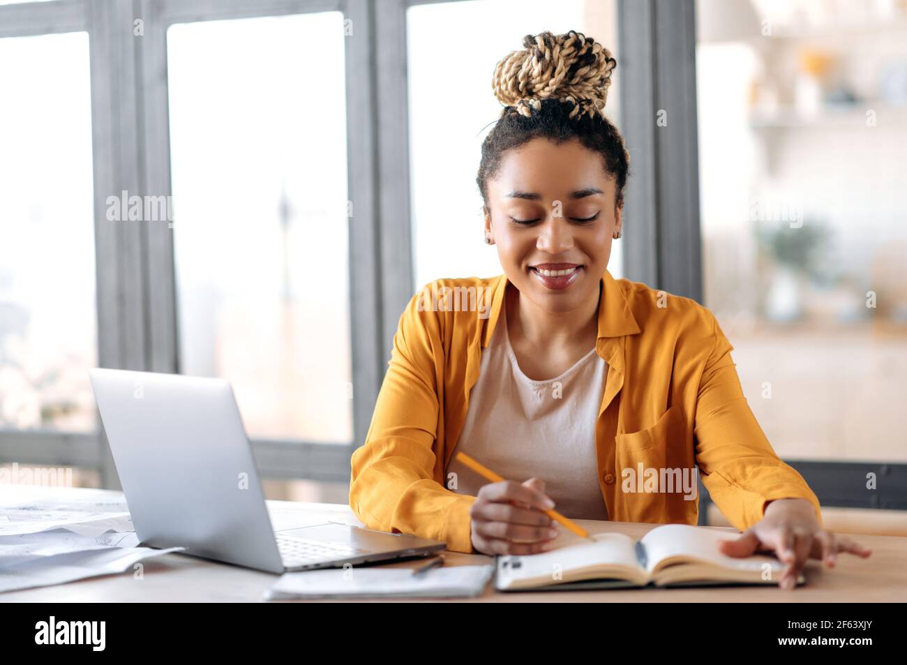 Online-Schulungen. Fröhlich clever fokussierten afroamerikanischen stilvolle junge Frau mit Dreadlocks, Student, Online-Studium zu Hause, Online-Video-Unterricht, nutzt Laptop, Notizen machen, Lächeln Stockfoto