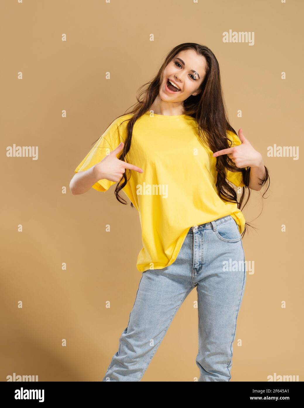 Ein fröhliches Mädchen zeigt mit ihren Fingern ein gelbes T-Shirt am Körper. T-Shirt-Modell. Stockfoto