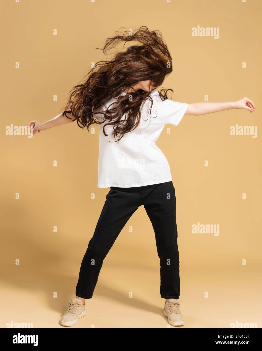 Junge schlanke Mädchen in einem weißen T-Shirt tanzen und winken lange Haare auf einem pastellorange Studio Hintergrund. Stockfoto