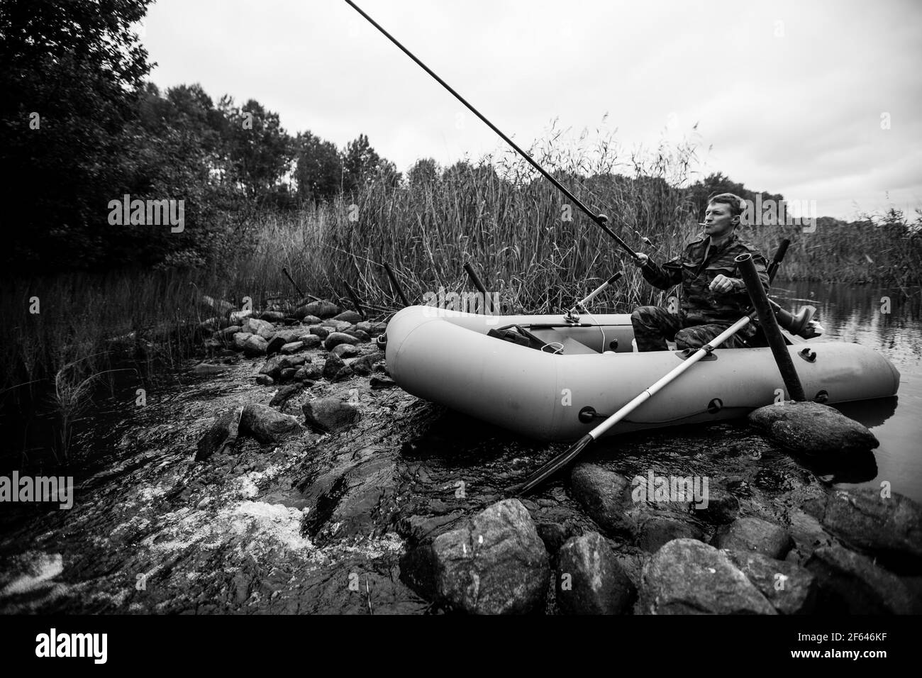 Ein Mann auf einem Gummiboot, der Fische auf dem See fängt. Schwarzweiß-Foto. Stockfoto