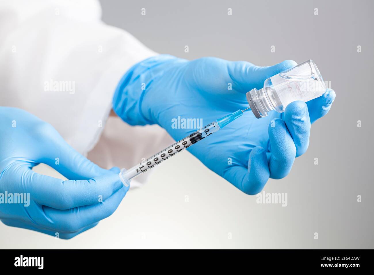 Nahaufnahme isoliertes Konzeptbild für einen Arzt, der flüssige Medikamente oder Impfstoffe aus einem Glasfläschchen mit Saugkappe in eine Spritze saugt. Stockfoto