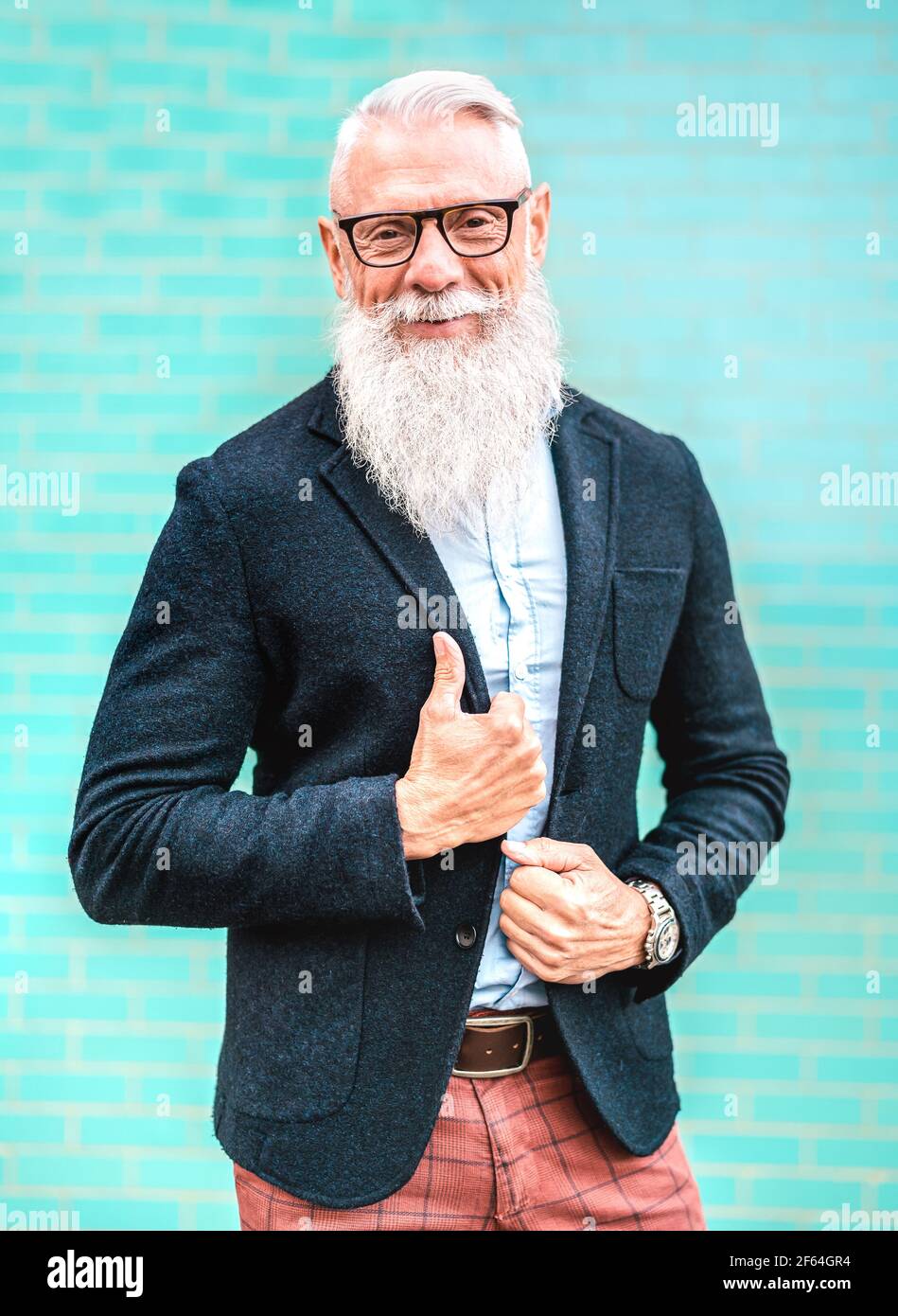 Vertikales Porträt eines Hipster-Mannes mit elegantem Outfit, gegen das er posiert Türkisfarbener Wandhintergrund - trendige alte Menschen tragen lässige Mode Stoff Stockfoto