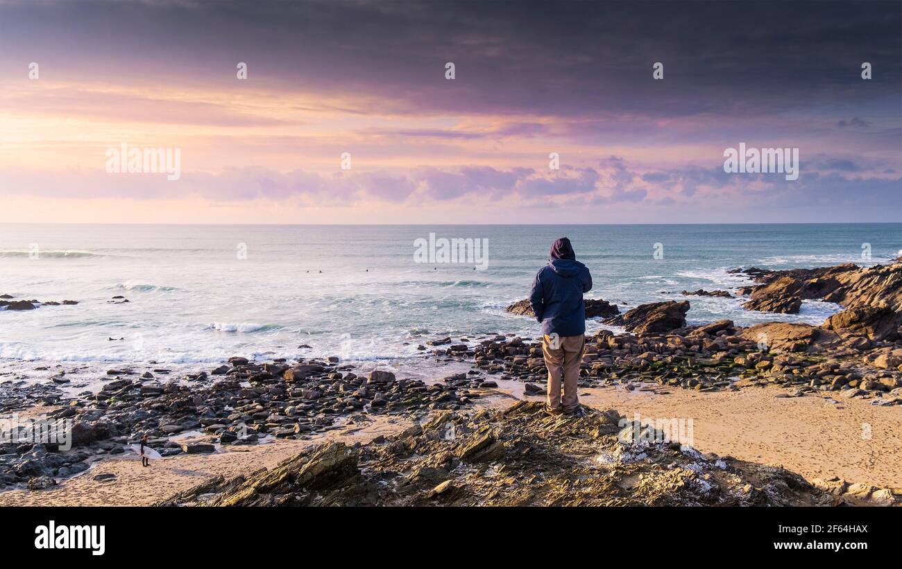 Ein Panoramablick auf einen Mann, der auf Felsen steht und auf das Meer bei Little Fistral in Newquay in Cornwall blickt. Stockfoto