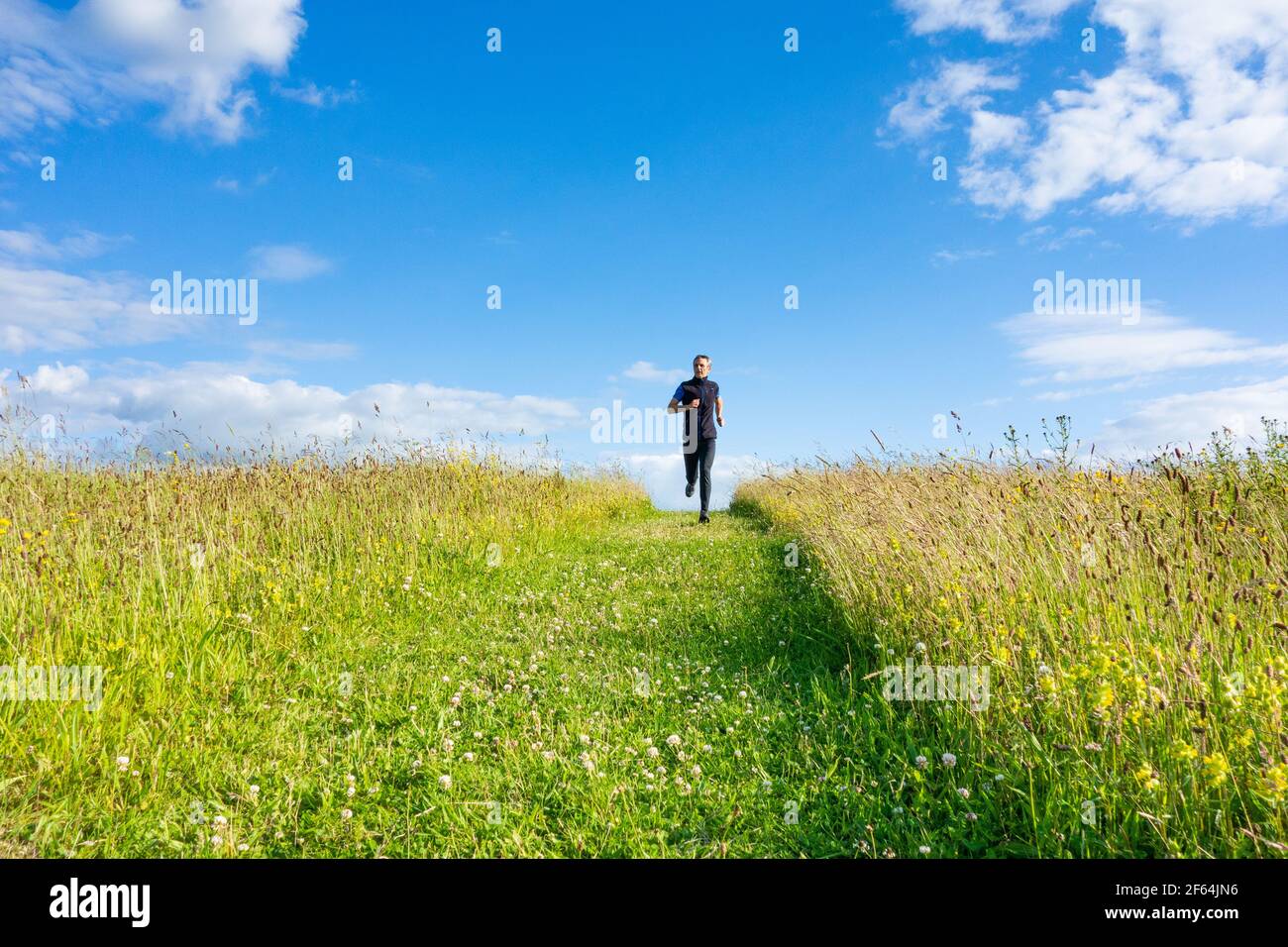 Reifer Mann läuft, joggt bergab auf dem Grasfußweg auf dem Hügel in der Landschaft. VEREINIGTES KÖNIGREICH Stockfoto
