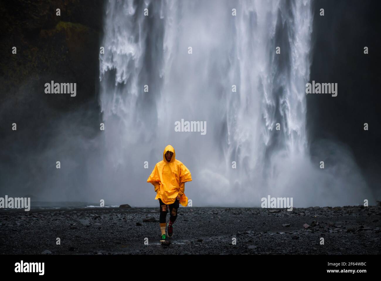 Touristische trägt einen gelben Regenmantel Wanderungen von der Skogafoss Wasserfall in Island Stockfoto