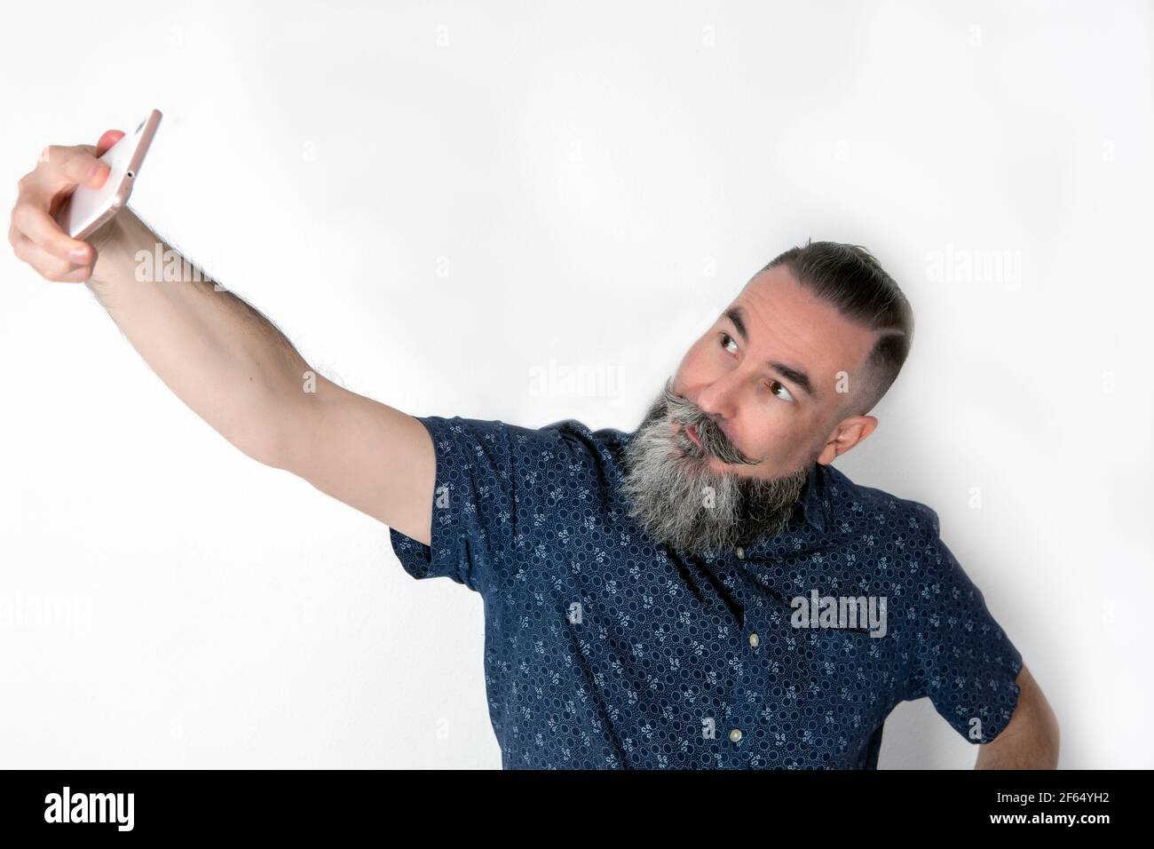 40-45-jähriger Mann mit einem großen, mittelgrauen Bart, der sein Smartphone benutzt, um ein Selbstporträt zu machen (Selfie) Stockfoto