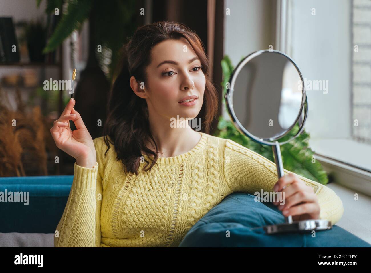 Junge hübsche Frau macht Make-up zu Hause beim Blick in Der Spiegel Stockfoto