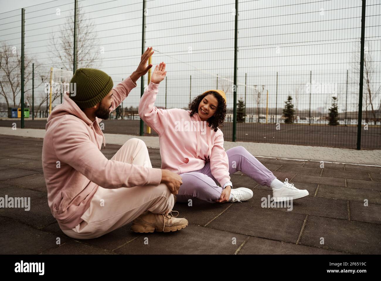Aufgeregt afroamerikanische Freunde in Sportswear geben High fünf während Sitzen auf Sportplatz Stockfoto