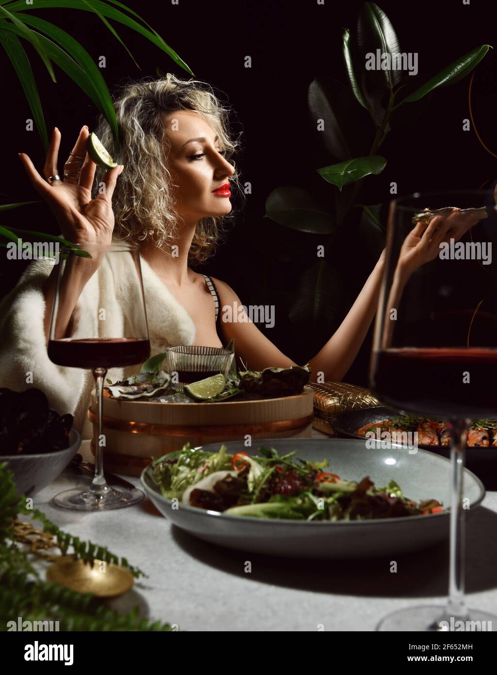 Junge blonde Frau in Abendkleid mit tiefem Ausschnitt und Pelz sitzen in Meeresfrüchte-Restaurant auf einem Date Stockfoto