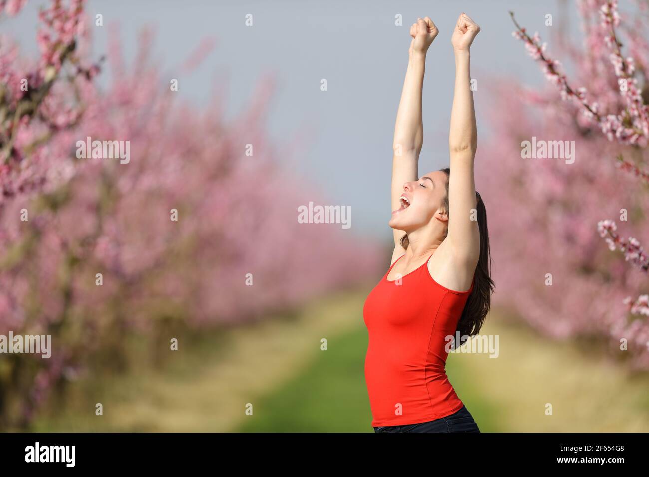 Aufgeregte Frau in rot, die Arme mit gewachsten Achselhöhlen aufhebt Ein Feld, das Urlaub feiert Stockfoto