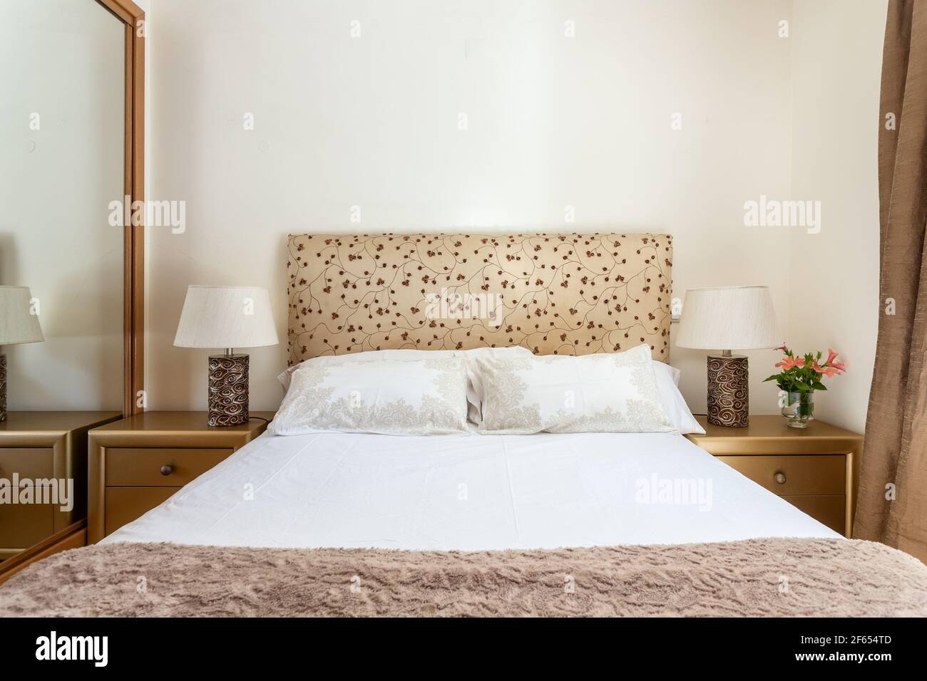 Das Zimmer war sauber und schlicht und hatte beigefarbene Farben, ein weißes Bett mit Kissen und einen Nachttisch auf jeder Seite. Immobilien. Stockfoto