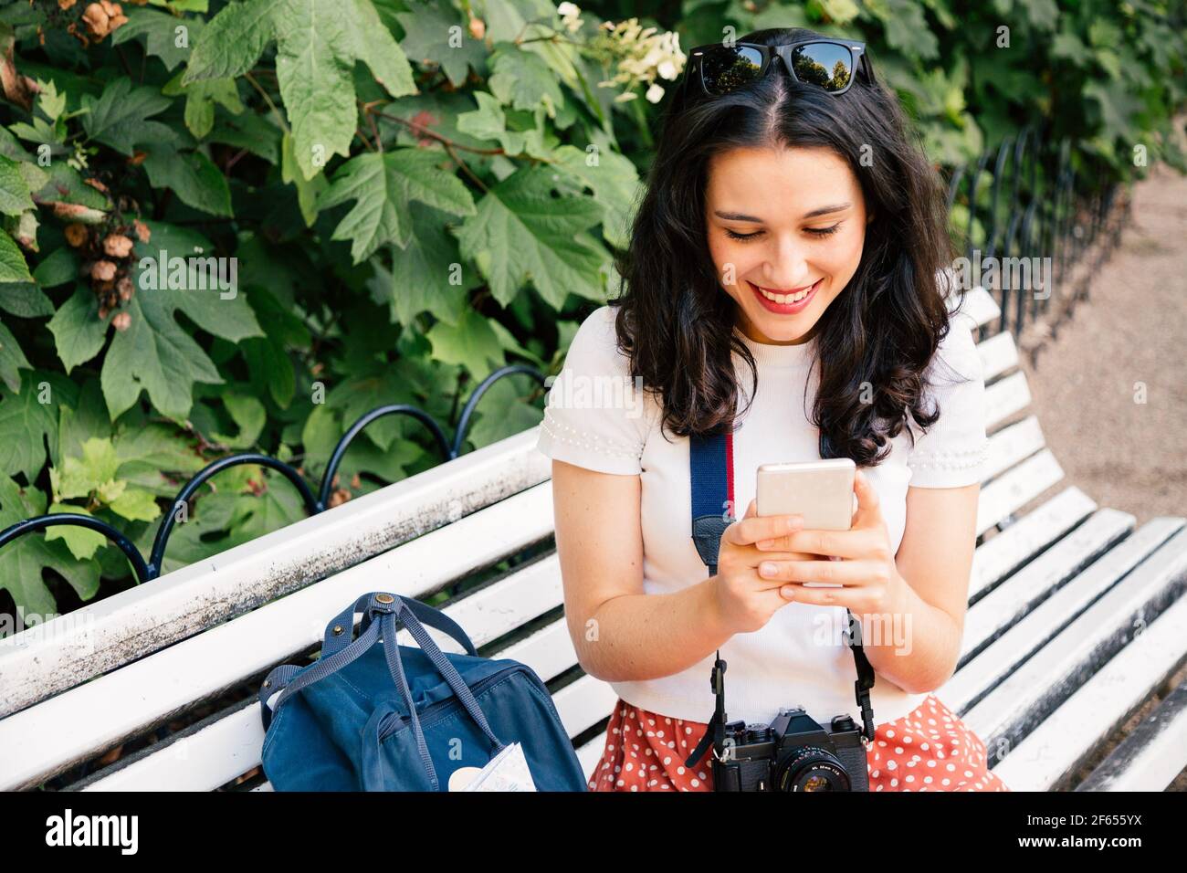 Glückliche Touristenfrau mit ihrem Martphone auf einer Parkbank sitzend. Süchtig nach Technologie Stockfoto