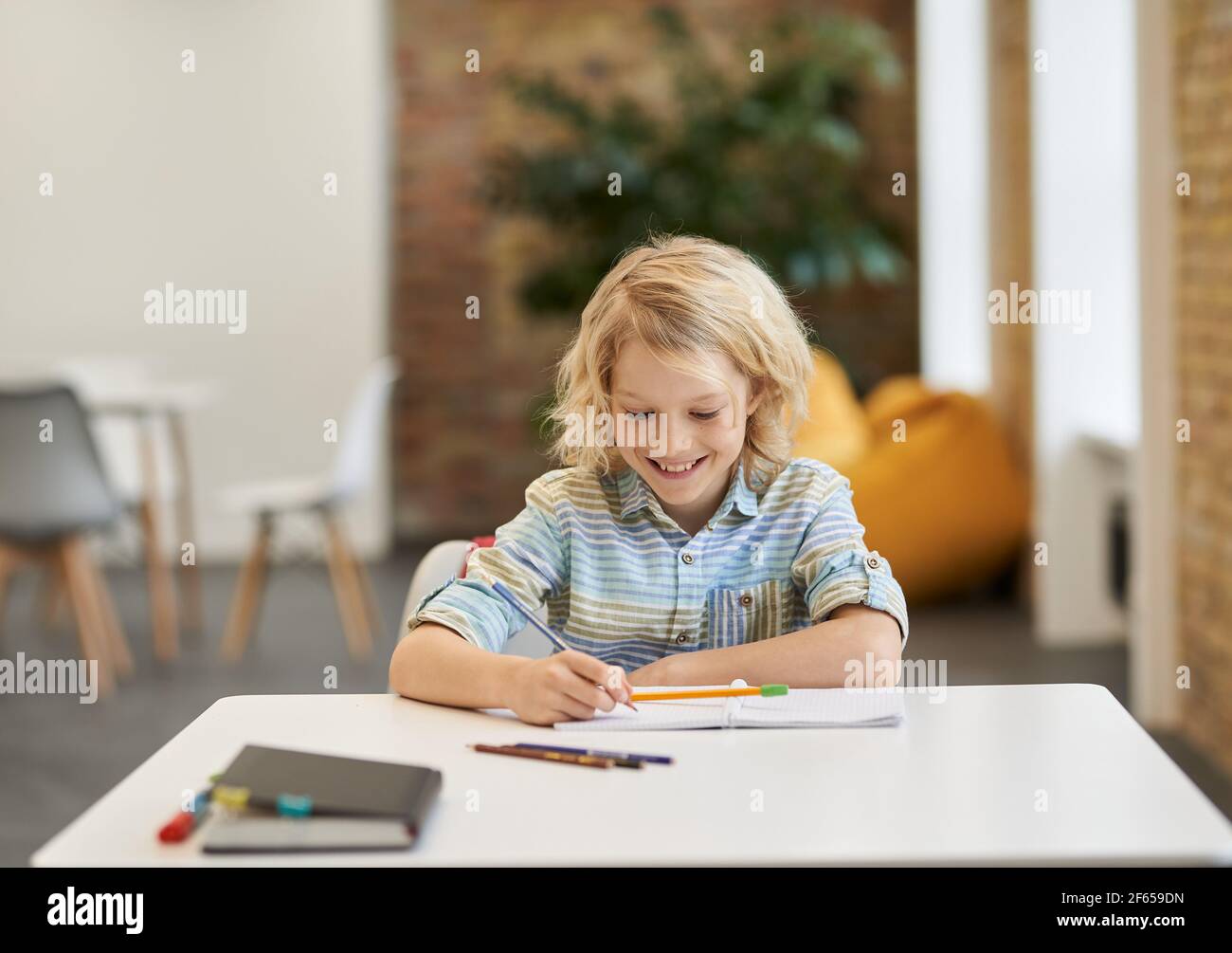 Aufgeregt Schuljunge lächelnd und tut Summen, schriftlich in seinem Notebook, während am Schreibtisch im Klassenzimmer sitzen Stockfoto