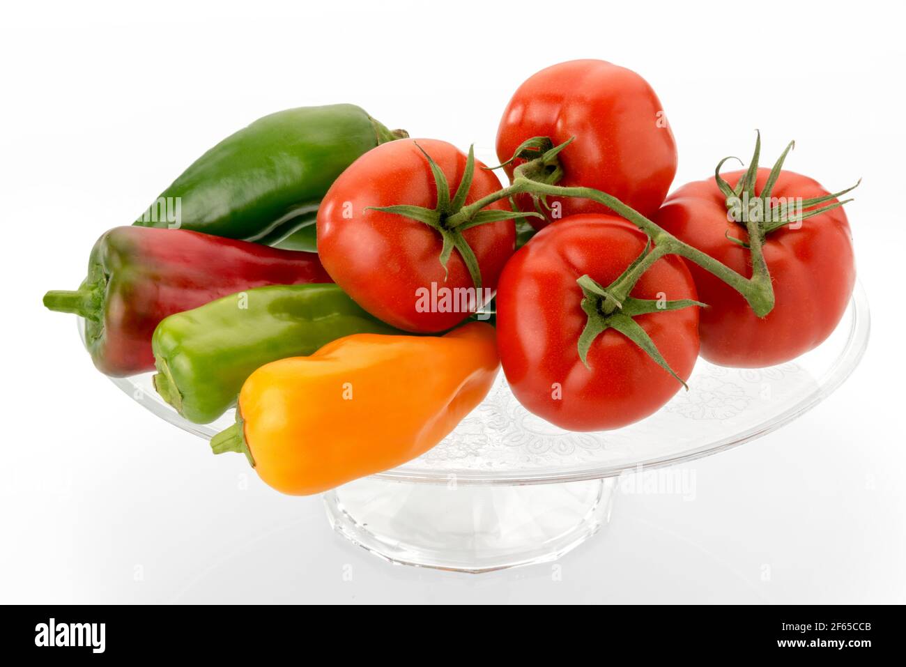 Tomaten und Paprika auf klarem Glas erhöhte Platte - rot, gelb und grün Gemüse isoliert auf weißem Hintergrund Stockfoto