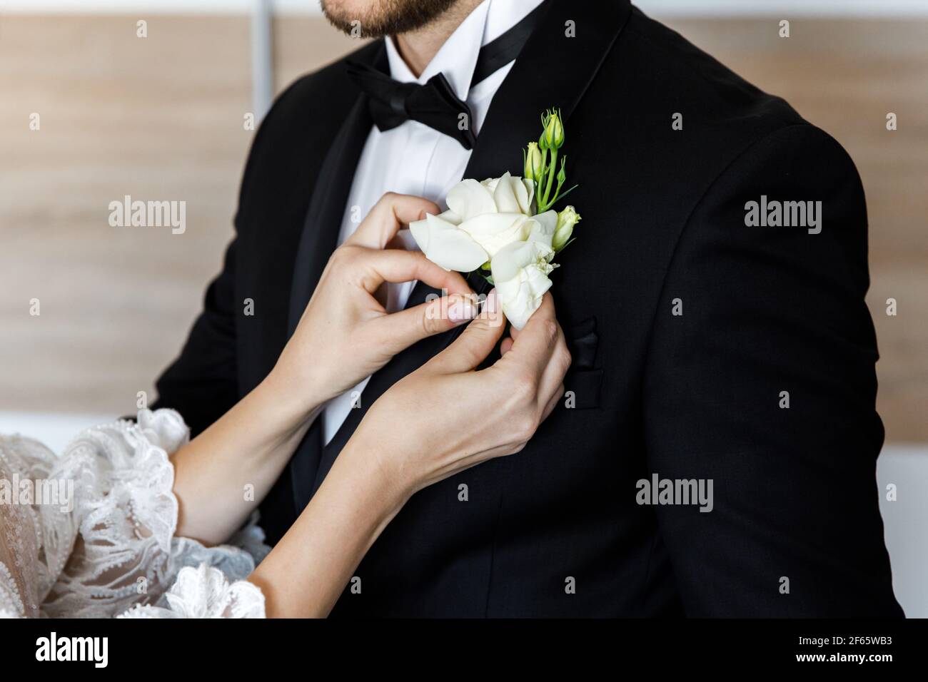 Hübsche junge Braut, die ihr einen zarten Knopfloch-Strauß festlegt Jacke des Bräutigams Stockfoto