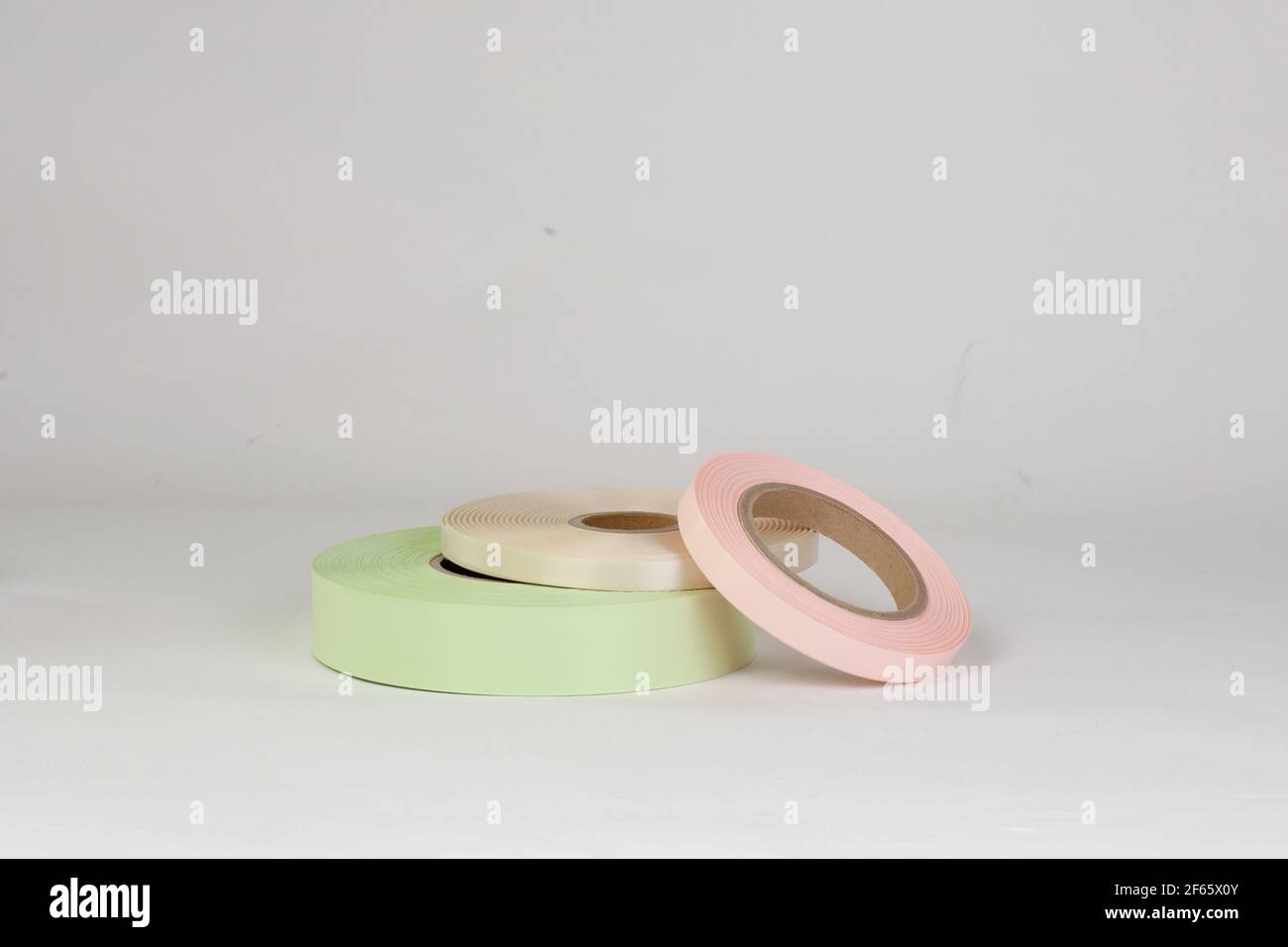 Zusammensetzung von drei Spulen von Satinbändern in rosa, grün, beige für Tags oder Branding, isoliert auf einem weißen, grauen Hintergrund Stockfoto
