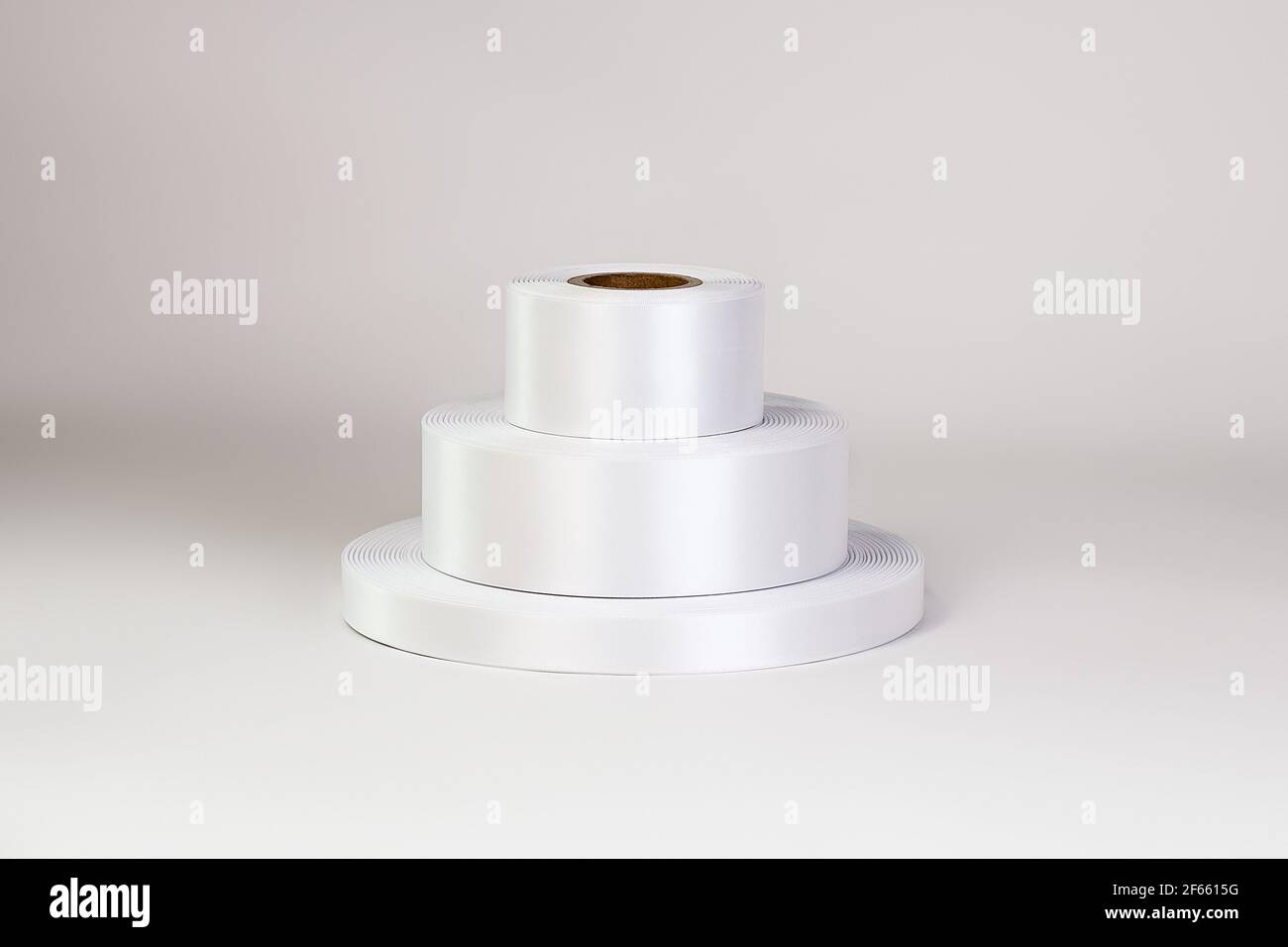 Ein Turm aus drei Spulen von weißen Satinbändern in verschiedenen Größen für Etiketten oder Branding, isoliert auf einem weißen, grauen Hintergrund Stockfoto