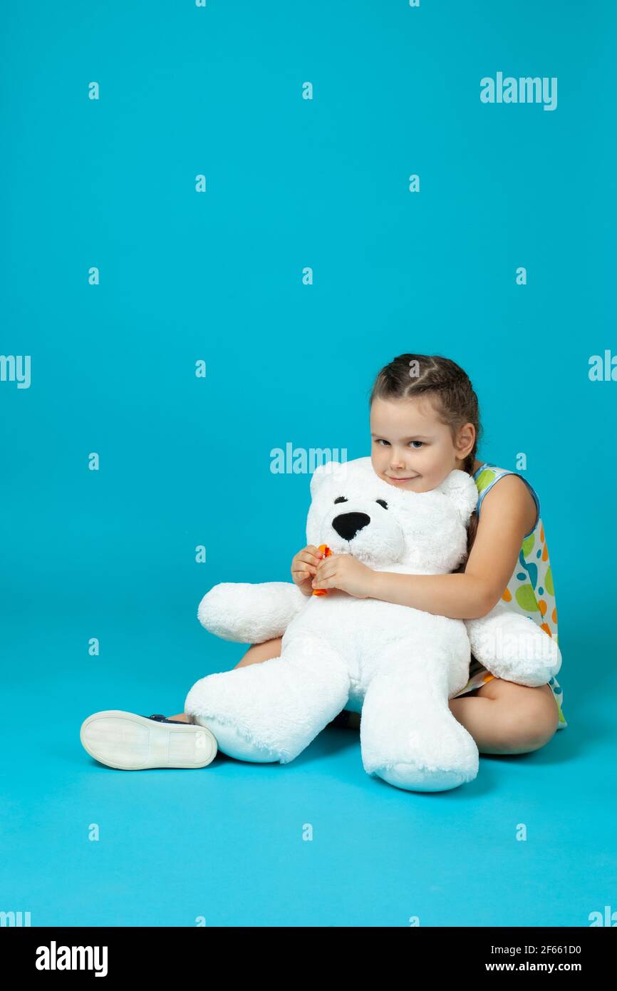 Porträt eines Mädchens, das auf dem Boden sitzt, einen weißen Teddybären umarmt und einen Zahnarztmann mit einer auf blauem Hintergrund isolierten Pinzette herauszieht Stockfoto