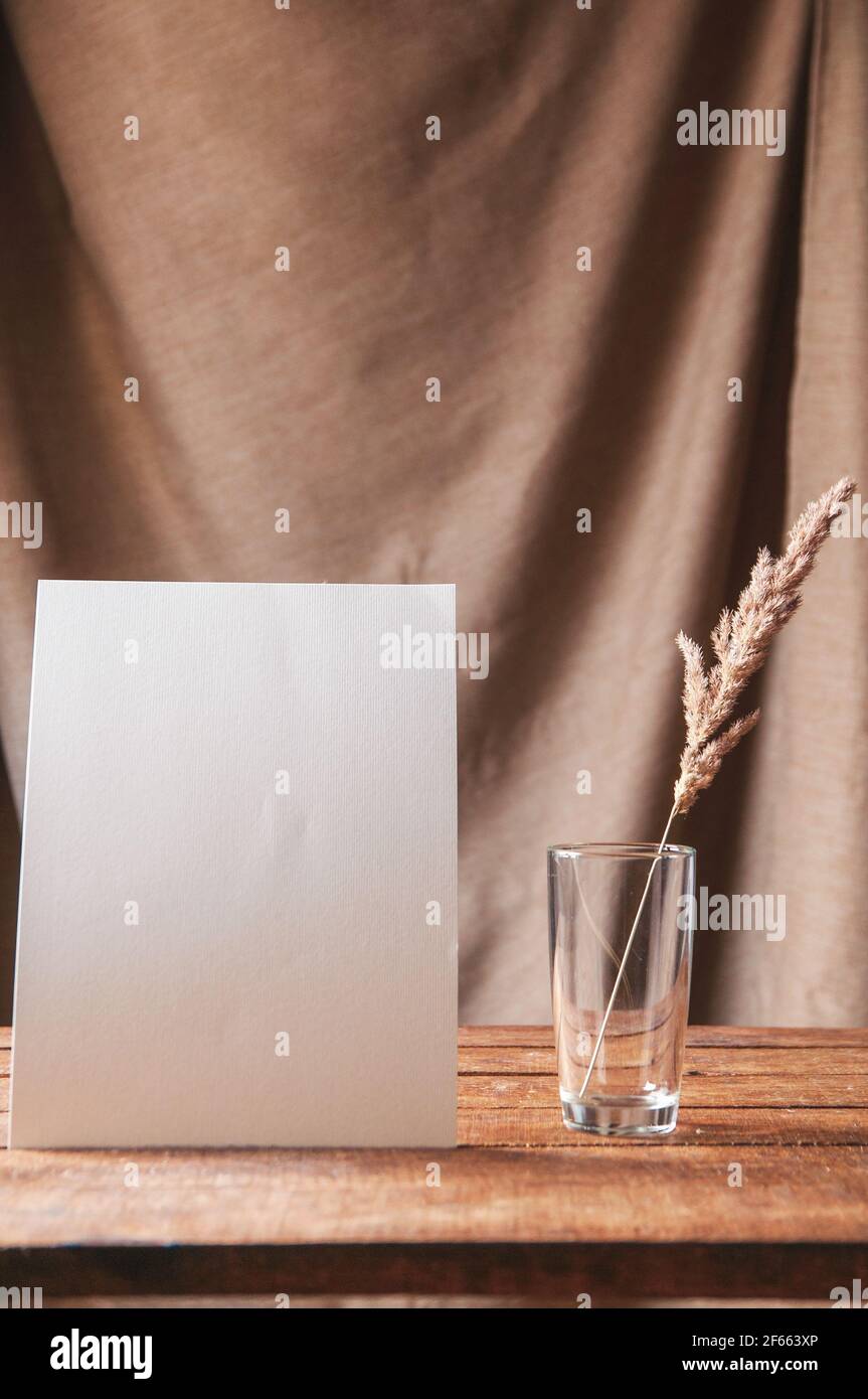 Auf dem Tisch ist ein weißes Blatt Papier mit getrockneten Blumen in einem Glas. Für eine Designpräsentation oder ein Portfolio. Stockfoto