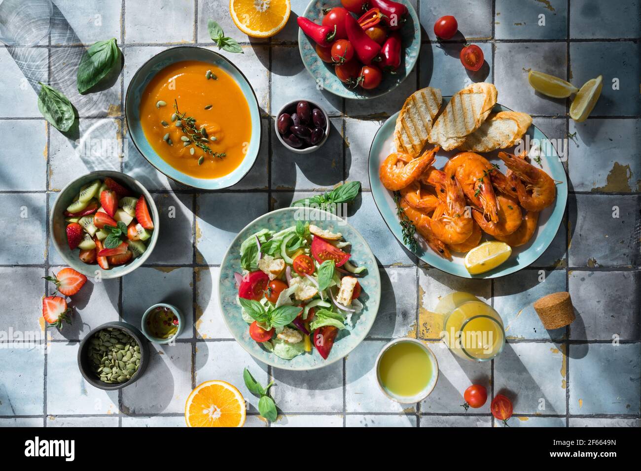 Mediterrane Gerichte am Kacheltisch: Meeresfrüchte-Garnelen, Gemüsesalat, Kürbissuppe, Samen und Fruchtlimonade Stockfoto