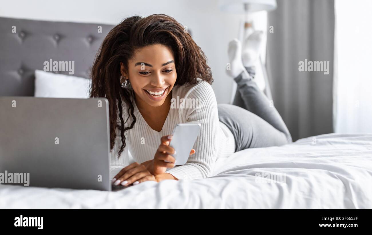 Glückliche schwarze Frau liegt im Bett und liest SMS Stockfoto