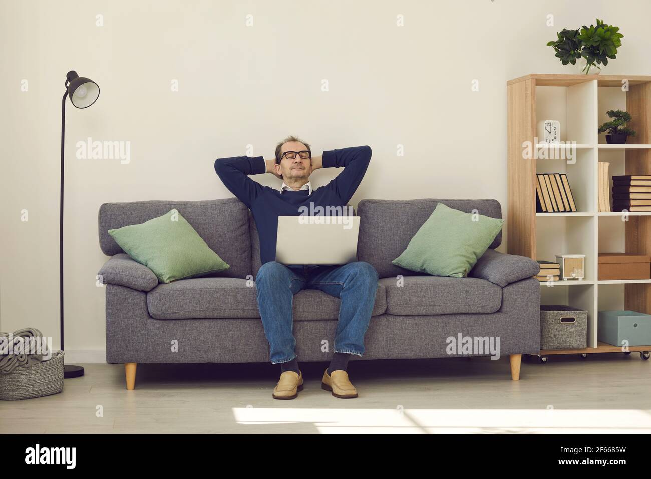 Ruhiger reifer Mann mit geschlossenen Augen entspannend auf bequeme Couch Mit Laptop Stockfoto
